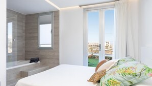 A modern bedroom with a large bed, a shower area, and a balcony with a view of buildings. - Spacious ground floor apartment with large terrace and sea views in Costa Adeje (Adeje)