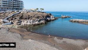 Et kysthotel med en klippefyldt kystlinje, klart blåt hav og en sti til stranden.