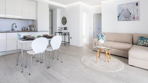 Et moderne køkken med hvide skabe, et spiseområde med hvide stole, og en beige sofa i en stue.