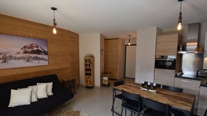 Una cocina moderna con electrodomésticos de acero inoxidable, una mesa de comedor de madera con sillas y un sofá negro con una alfombra de piel.