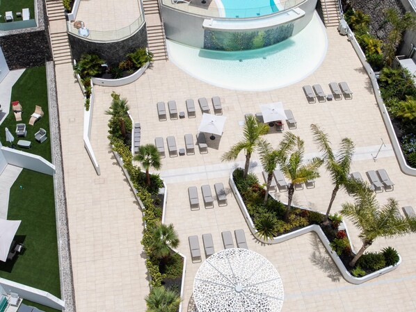 An aerial view of a resort with a pool, sun loungers, and a circular seating area.