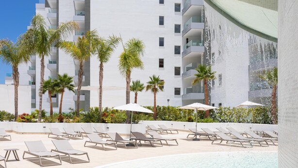Un espace piscine moderne avec des chaises longues et des palmiers.