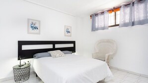 Een slaapkamer met een bed, een stoel, een nachtkastje en twee foto’s aan de muur.