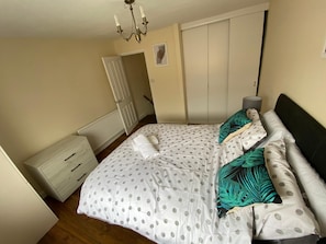 A bedroom with a bed, a nightstand, a dresser, a door, and a ceiling light.