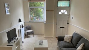 A living room with a TV, a grey sofa, a white coffee table, and a window with a view of trees. - Reading 3 Bedroom apartment (Reading)