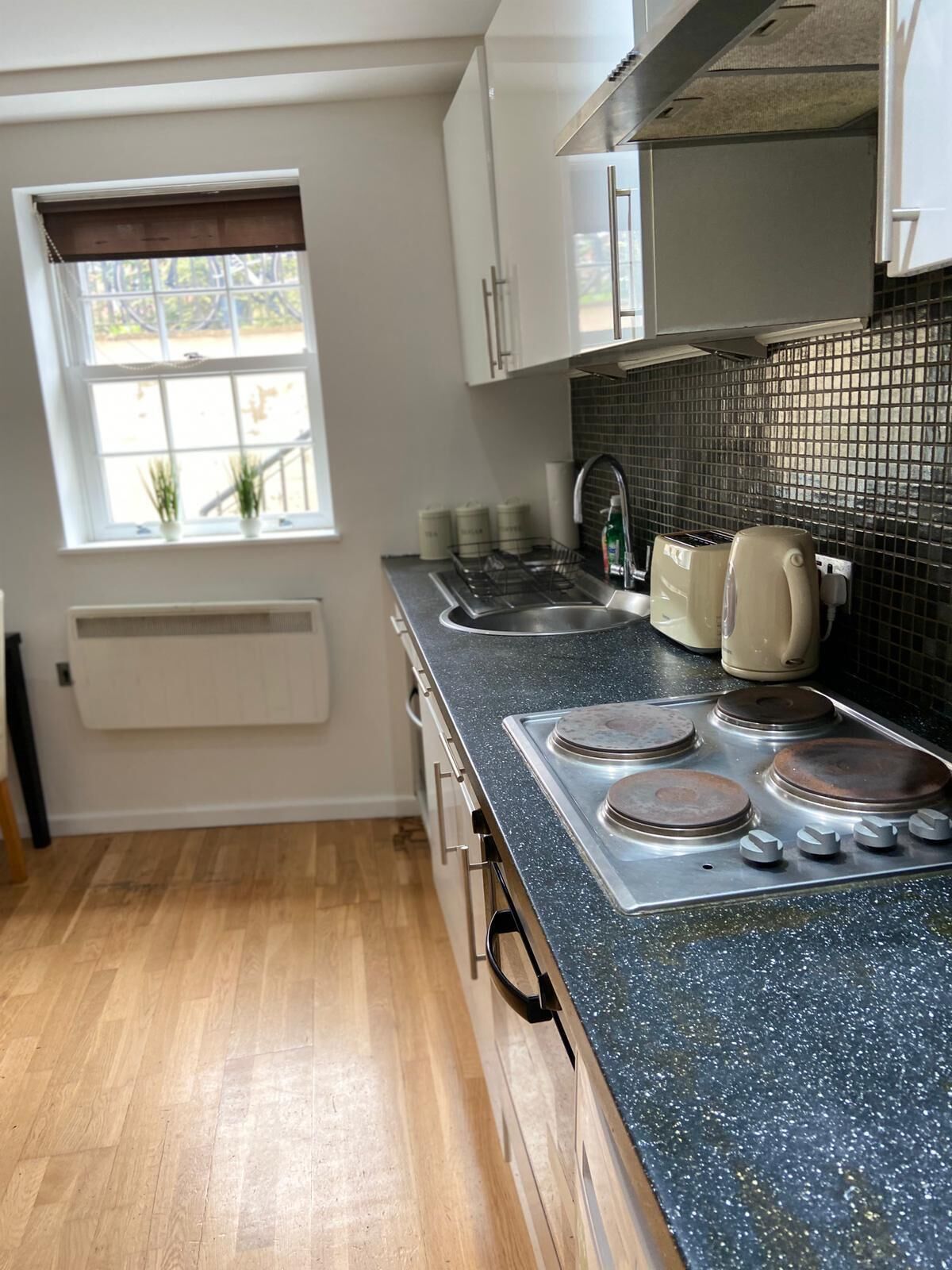 A compact kitchen with a gas stove, a sink, and a window with blinds.