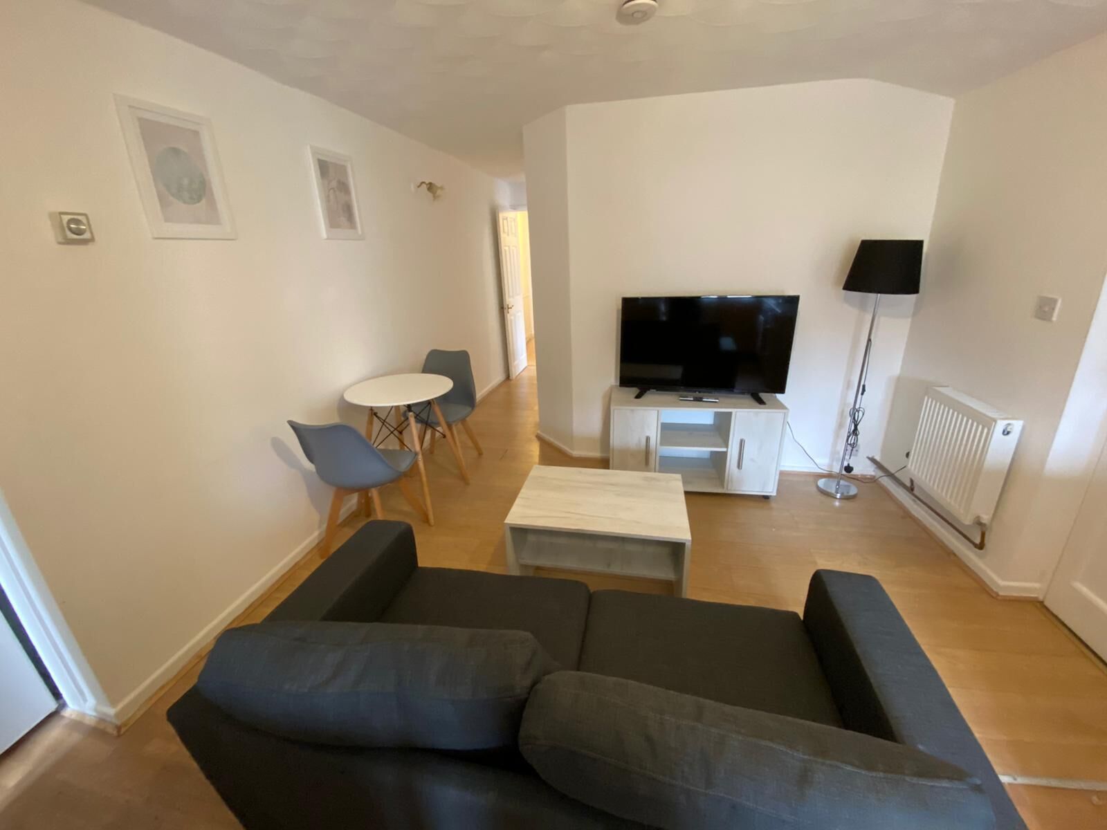A modern living room with a black sofa, a white coffee table, a TV on a white stand, and a dining area with a small table and chairs.