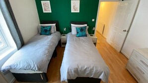 A twin room with two beds, a green accent wall, and a white wardrobe. - 3 Bedroom Apartment (Reading)