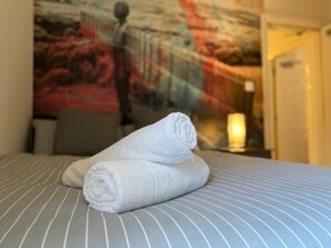 Un lit bien fait, recouvert d’une couvre-lit à rayures, avec deux serviettes blanches roulées posées dessus.
