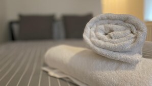 Een keurig opgemaakt witte handdoek op een gestreept bed, met twee kussens op de achtergrond.