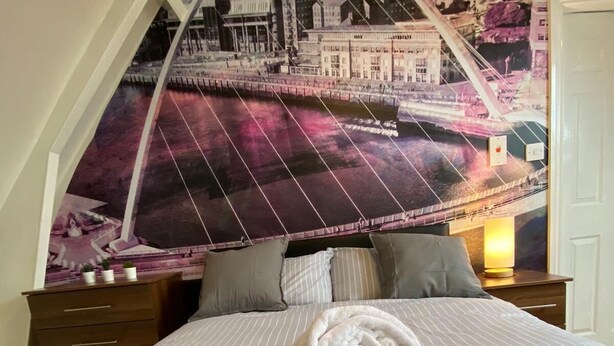 Een hotelkamer met een bed, nachtkastje, lamp en een groot stadsgezicht muurdecoratie.