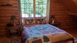 Un dormitorio acogedor con una cama grande, paredes de madera y una ventana con vistas a árboles.