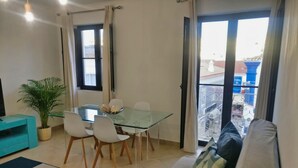 Una sala de estar moderna con una mesa de comedor de vidrio, sillas blancas, un sofá azul verdoso y una planta en maceta.