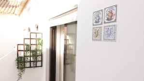 A white wall with a sliding glass door, a wooden shelf with plants, and four decorative tiles. - Old Town Apartments 2D (Albufeira)