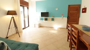 A living room with a sofa, a television on a stand, a dining table with chairs, and a lamp. - Old Town Apartments 2D (Albufeira)