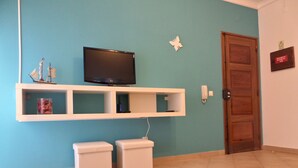 A room with a television on a white shelf, a wooden door, and a small white cabinet. - Old Town Apartments 2D (Albufeira)