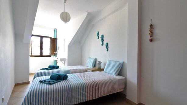 A bedroom with two beds, striped bedding, a hanging light fixture, and a decorative wall piece. - Old Town Apartments 2D (Albufeira)