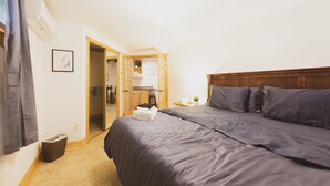 Une chambre avec un grand lit, une table de chevet, une lampe et une vue sur la cuisine.