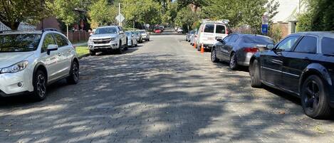 A paved street lined with parked cars and trees.