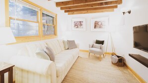 Un salon avec un canapé blanc, un petit fauteuil, un plafond en bois et une grande fenêtre.