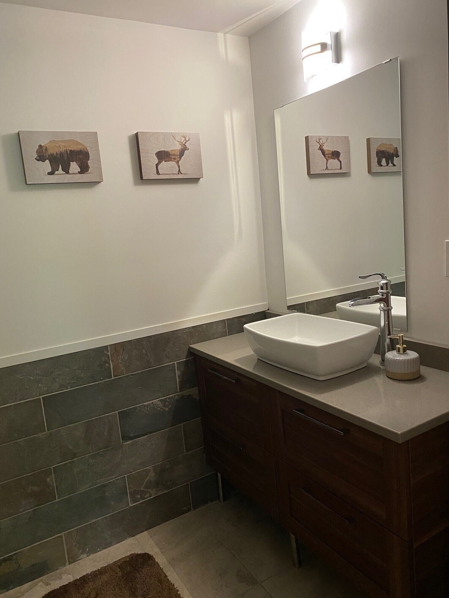 A bathroom with a white sink, dark wood cabinets, and a mirror above the sink. There are three animal-themed wall art pieces above the mirror.