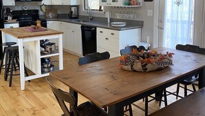 A modern kitchen with white cabinets, a black microwave, and a dining area with a wooden table and chairs. - Cozy Cabin Getaway - Convenient to 4 Ski Areas, Hiking and Mountain Bike Trails (Davis)
