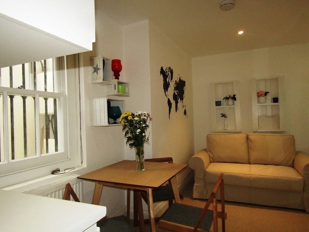 Un salon avec un canapé beige, une table en bois entourée de chaises, un vase rempli de fleurs et une carte du monde accrochée au mur.