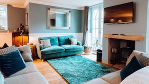 Una sala de estar con un sofá azul turquesa, un espejo grande, un televisor de pantalla plana y una chimenea.
