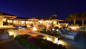Un área de piscina exterior bien iluminada con sillones de descanso y un bar.