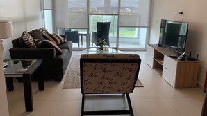 Un salon moderne comprenant un canapé, une table basse, un meuble pour la télévision et une grande fenêtre donnant sur la ville.