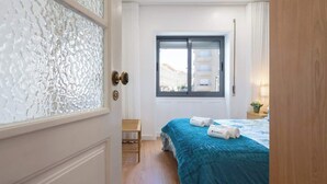 A hotel room with a bed, a window, and a door with frosted glass. - Anna´s Flats | Jardim do Morro by HostWise (Vila Nova de Gaia)