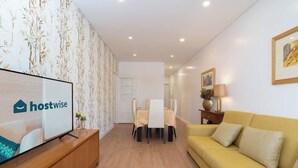 A modern living room with a sofa, a dining table with chairs, and a television on a wooden cabinet. - Anna´s Flats | Jardim do Morro by HostWise (Vila Nova de Gaia)