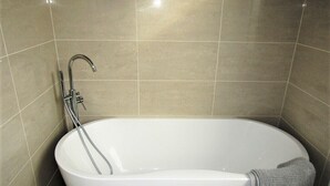 A modern bathroom with a freestanding bathtub, a handheld showerhead, and a towel on the side. - Large Private Double En-suite - 5 (London)