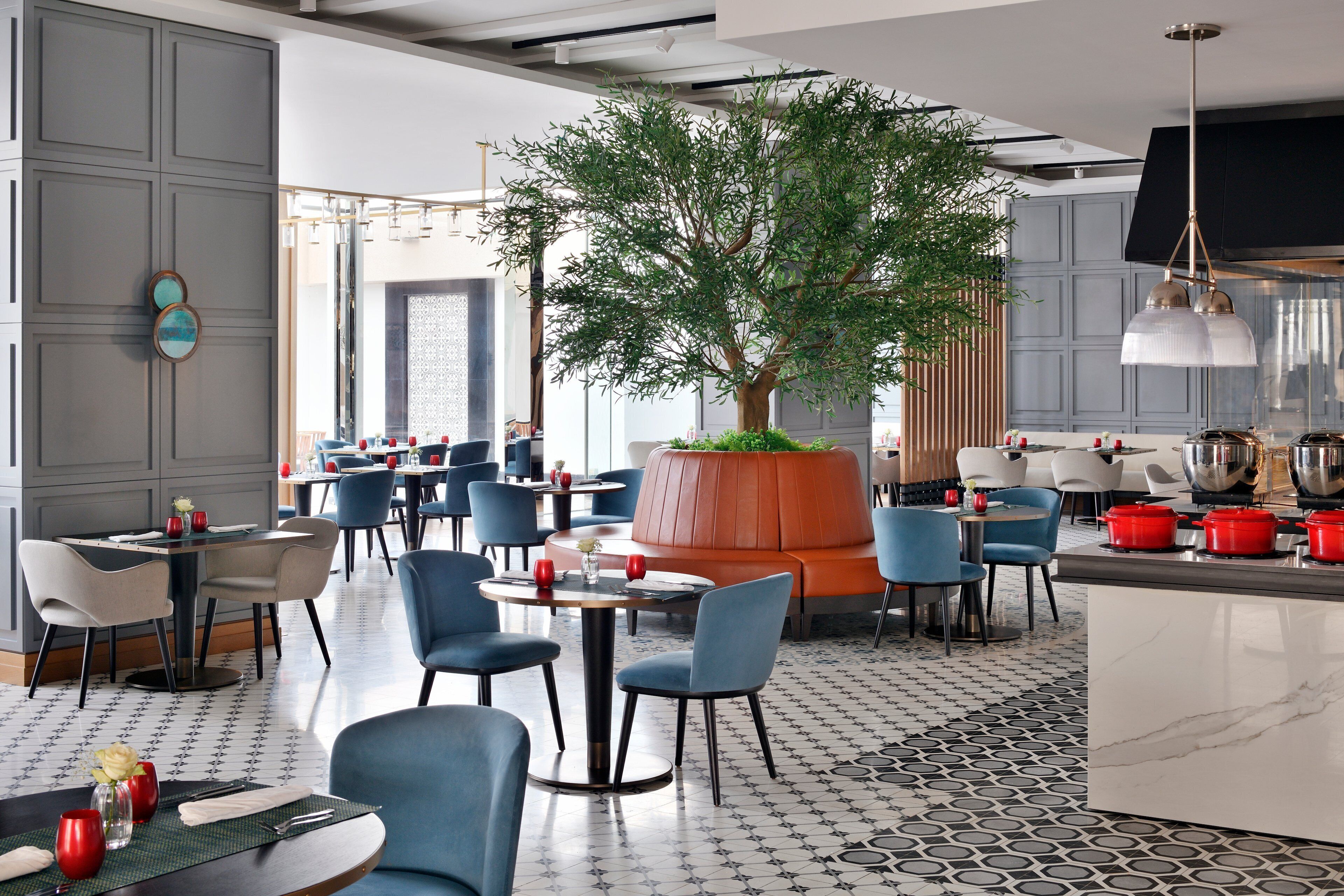 Un restaurante moderno con un jardín vertical central, sillas azules y blancas, y un suelo estampado.
