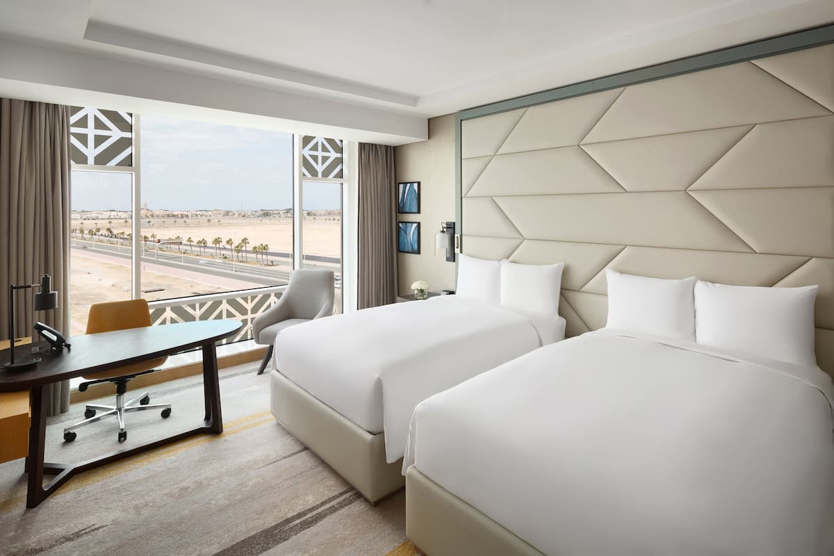 Une chambre d’hôtel avec deux lits, un bureau et une vue sur un paysage désertique.