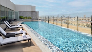 Una piscina infinita en la azotea con sillones de descanso y vistas a la ciudad.