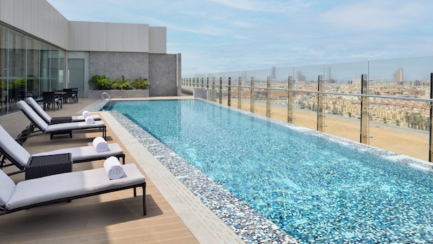 Une piscine à débordement située sur le toit, avec des chaises longues et une vue sur la ville.