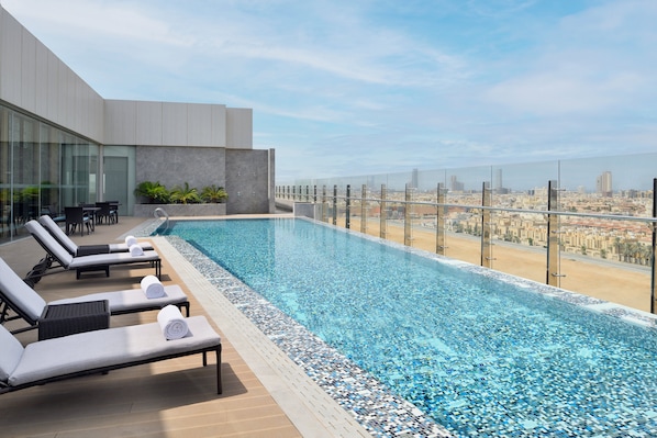 A rooftop infinity pool with lounge chairs and a city view.