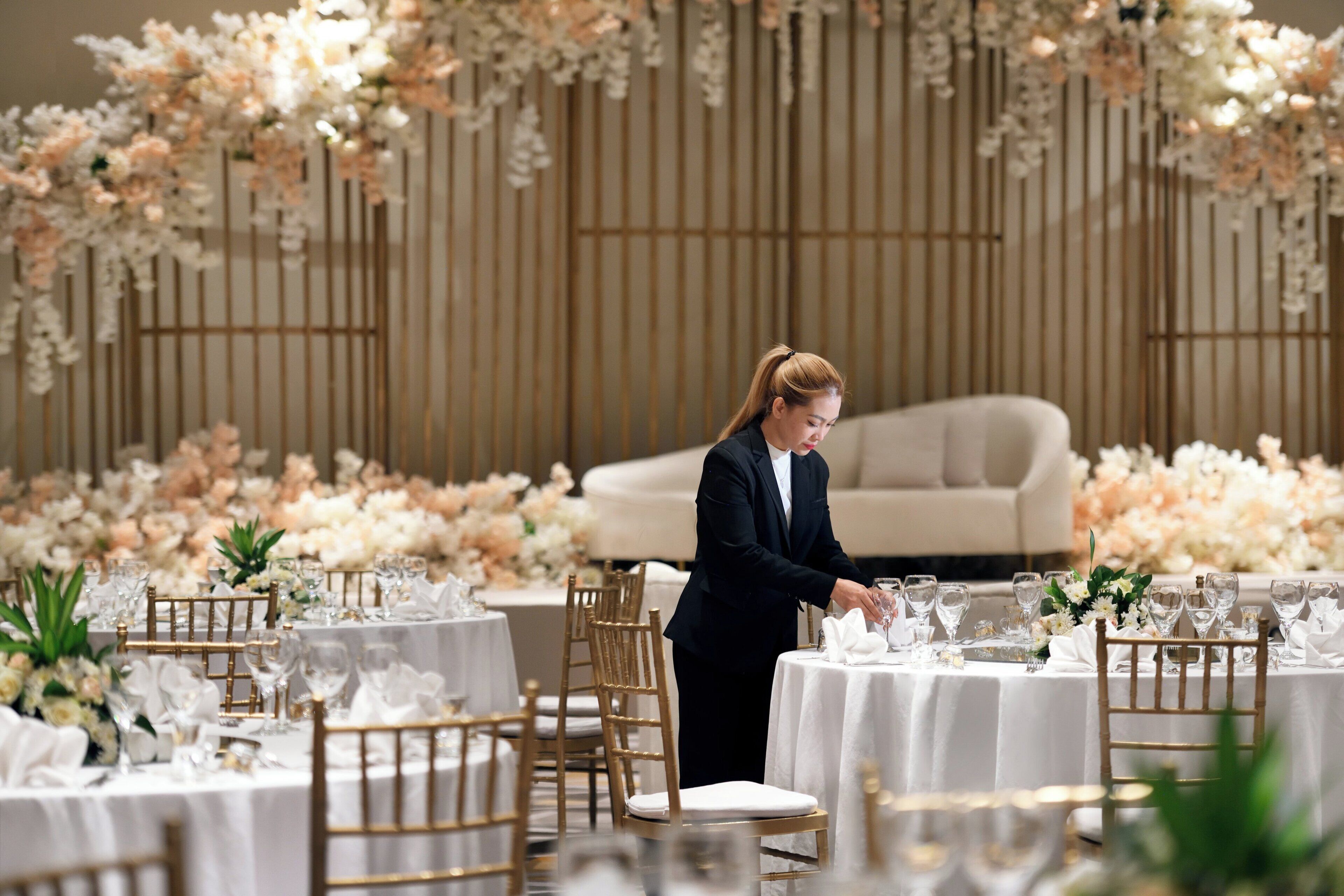 A formal dining setup with tables, chairs, and a person arranging glasses.
