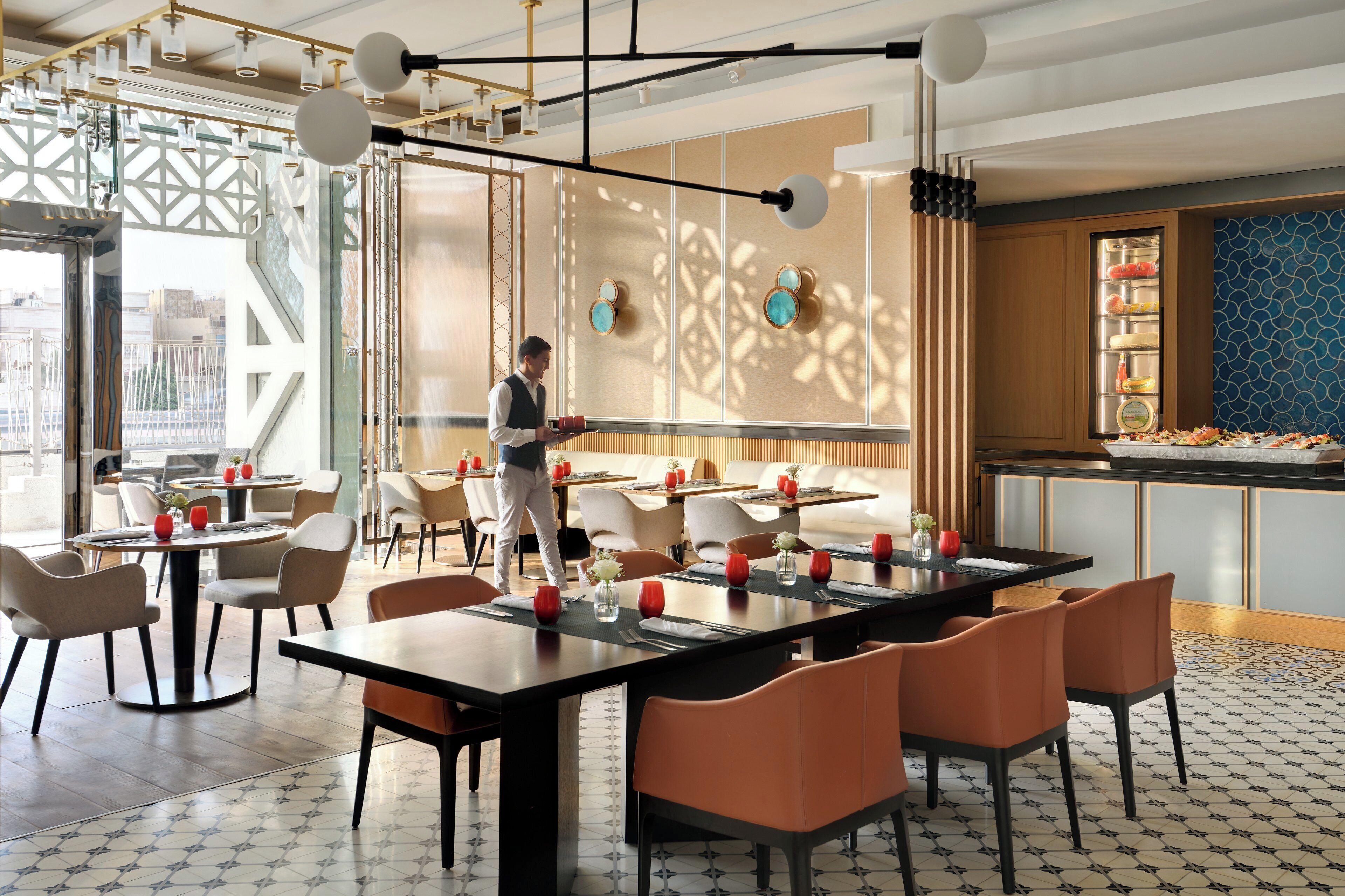 A modern restaurant with a waiter serving. Tables are set with red glasses and white napkins.