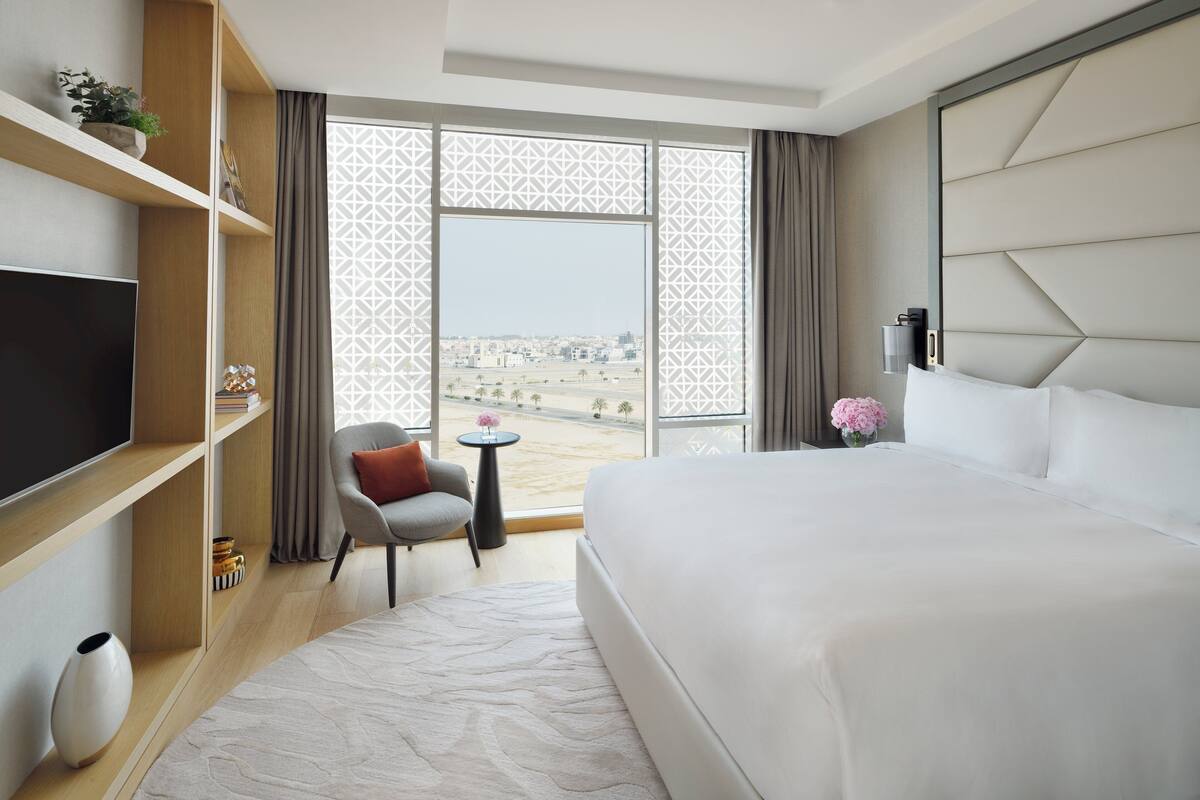 Une chambre d’hôtel avec un grand lit, une télévision, une petite table, une chaise et une vue sur la ville par une fenêtre à motifs.