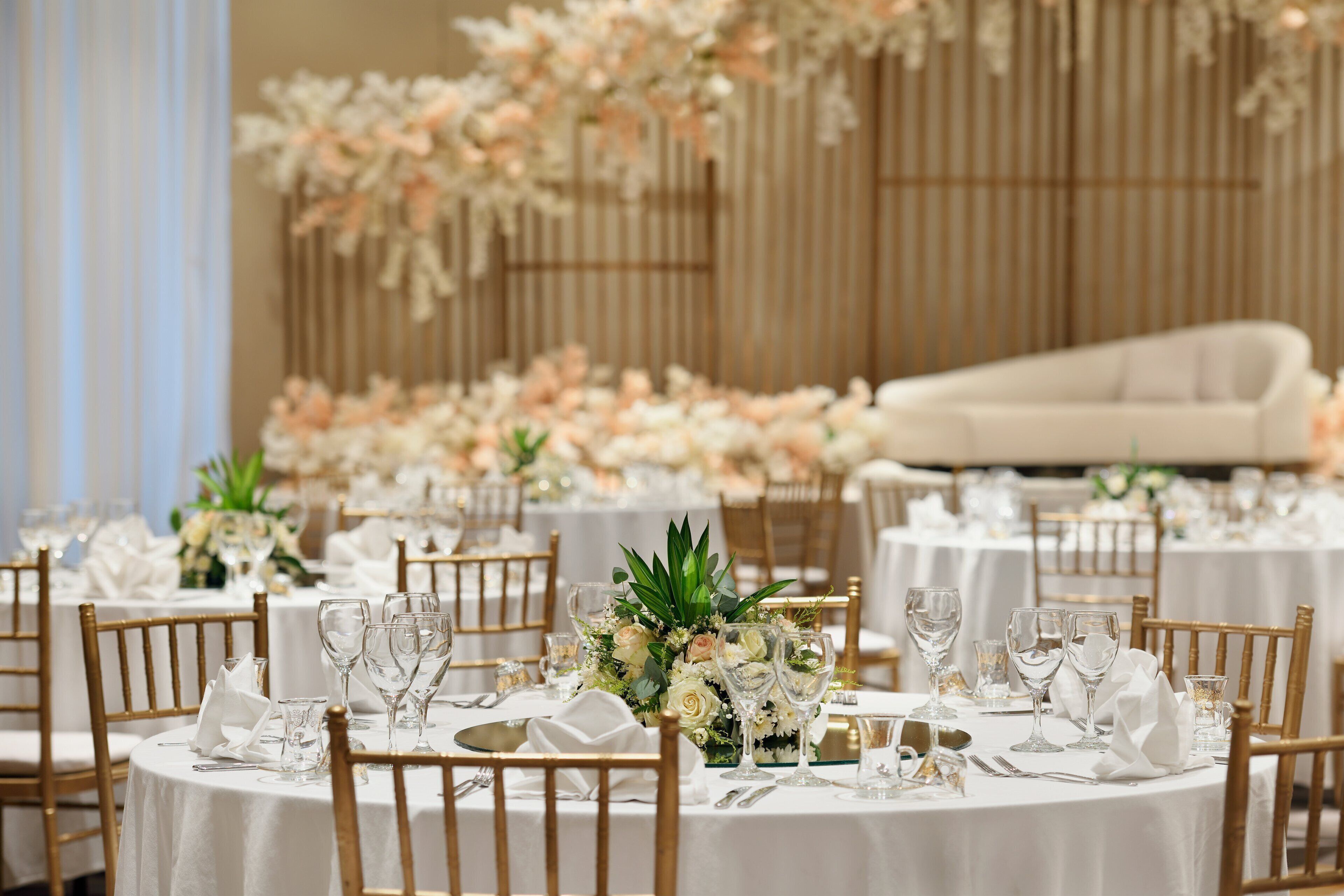 Un salón de banquetes con mesas redondas dispuestas para un evento formal, con manteles blancos, sillas doradas y centros de mesa florales.