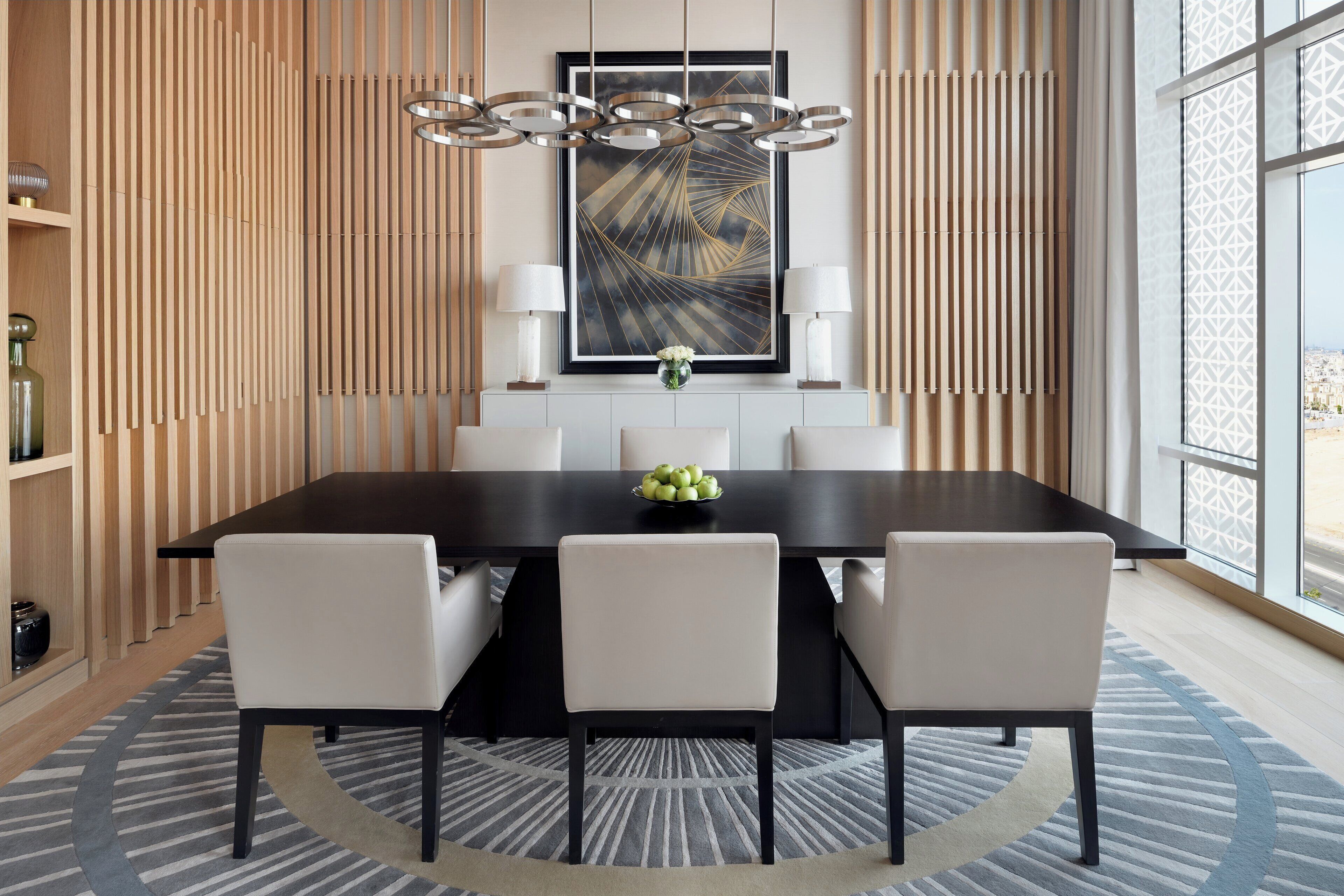 A modern dining area with a dark wooden table, white chairs, and a contemporary chandelier.