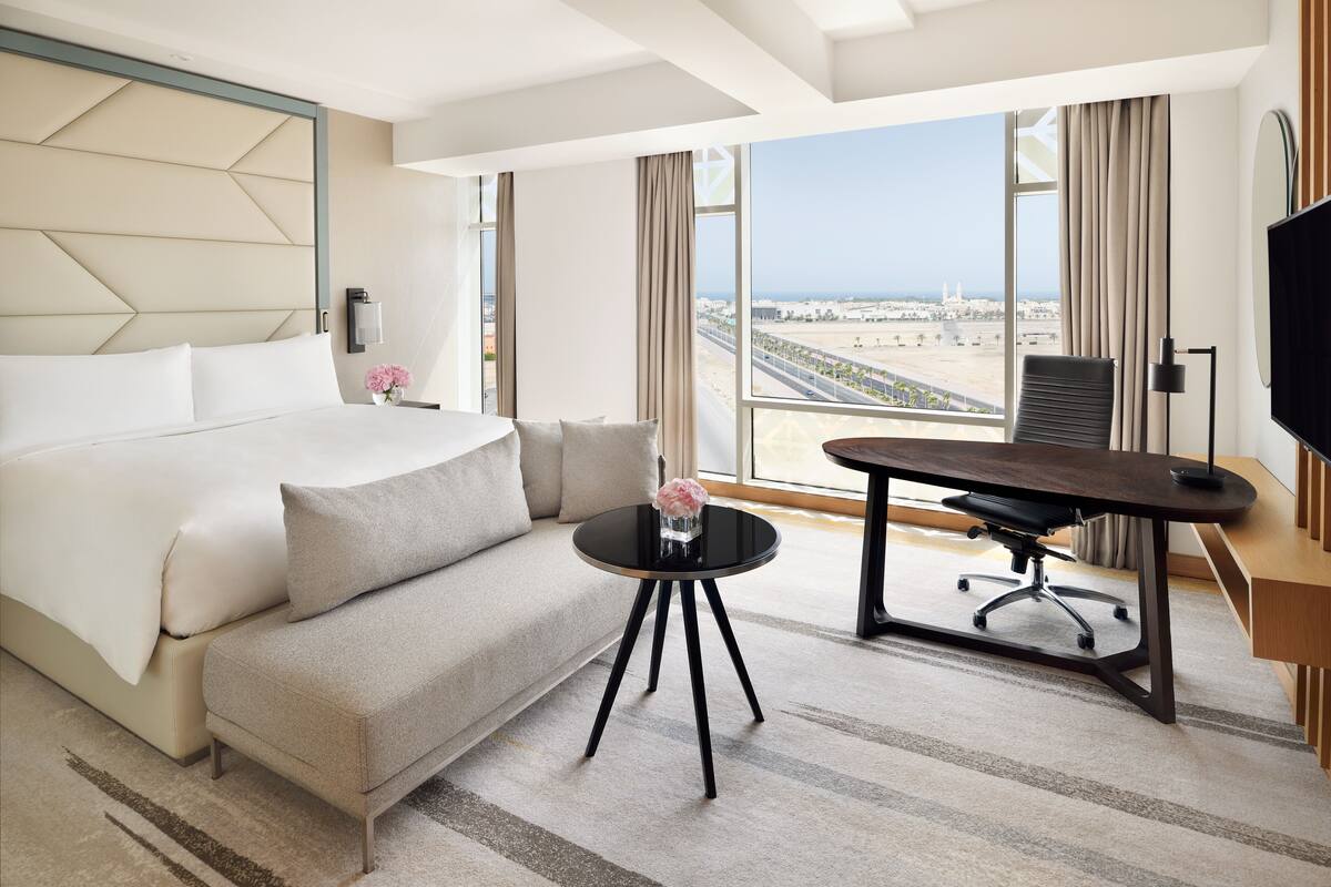 Une chambre d’hôtel avec un lit, un canapé, un bureau et une grande fenêtre donnant sur la ville.