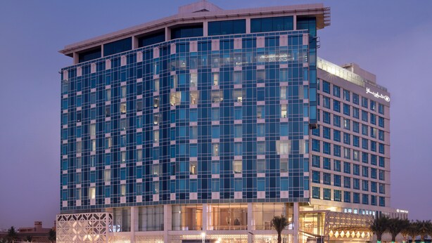 A modern hotel with a glass facade, multiple floors, and a prominent entrance with a covered area.