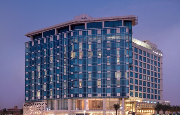 A modern hotel with a glass facade, multiple floors, and a prominent entrance with a covered area.