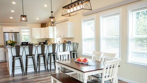 A modern kitchen with white cabinets, a wooden dining table, and bar stools. - Evergreen Lane Getaway · River Views and Front Porch Sitting in Paradise (Livingston)