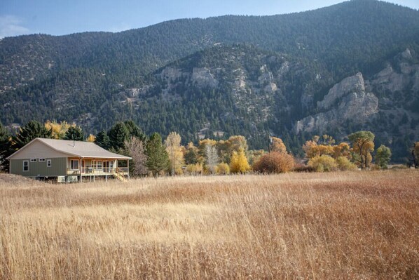 A house with a porch, surrounded by a field and mountains in the background. - Evergreen Lane Getaway · River Views and Front Porch Sitting in Paradise (Livingston)