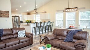 A modern living room with two brown leather sofas, a wooden coffee table, and a kitchen in the background. - Evergreen Lane Getaway · River Views and Front Porch Sitting in Paradise (Livingston)