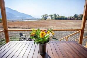 A wooden table with a vase of yellow flowers on a balcony overlooking a field and mountains. - Evergreen Lane Getaway · River Views and Front Porch Sitting in Paradise (Livingston)